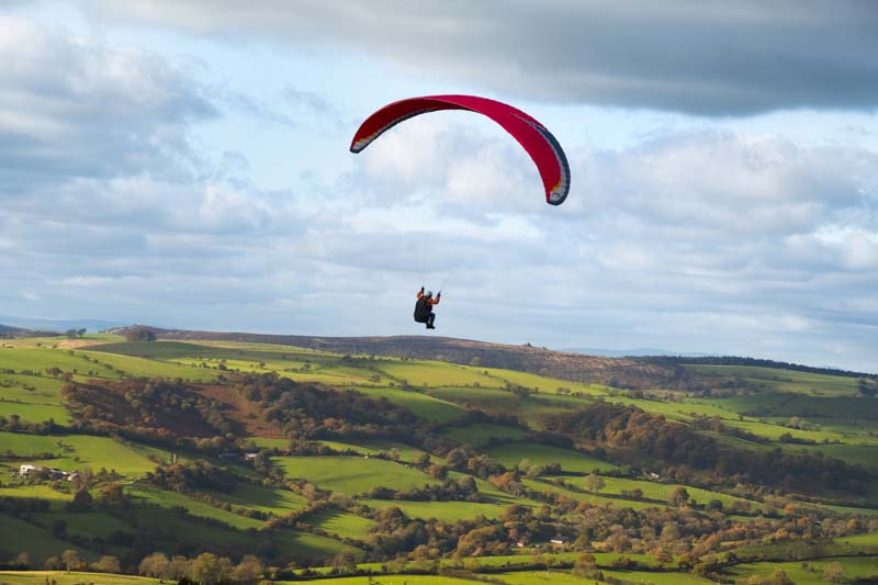 A paraglider soars over the Onny Valley, seen from the Long Mynd, Shropshire.